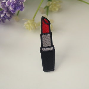 May include: An embroidered iron-on patch of a lipstick tube, in red and black.