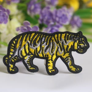 Könnte beinhalten: Gestickter Bügelaufkleber mit einem gelben und schwarzen Tiger. Der Tiger geht mit dem Kopf zur Seite gedreht.