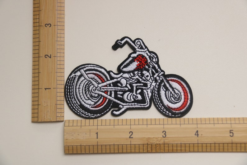 May include: White and red embroidered motorcycle patch. The motorcycle is a chopper style with a skull design on the gas tank.