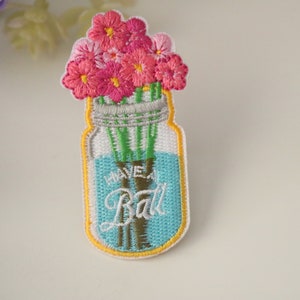 May include: Embroidered iron-on patch featuring a mason jar filled with pink flowers and the text "Have a Ball" in white.