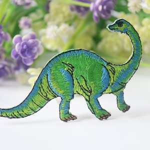 Peut inclure: Patch brodé de dinosaure vert et bleu. Le dinosaure a un long cou et une longue queue.