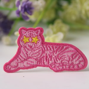 May include: Pink embroidered iron-on patch of a tiger with yellow star-shaped eyes.