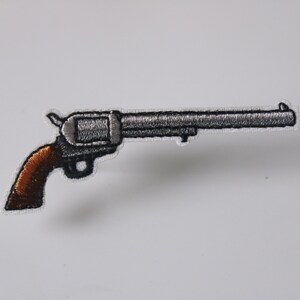 May include: A silver and brown embroidered patch of a revolver pistol.