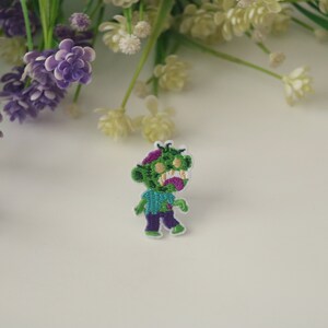 May include: Green and purple embroidered iron-on patch of a cartoon zombie with a toothy grin.