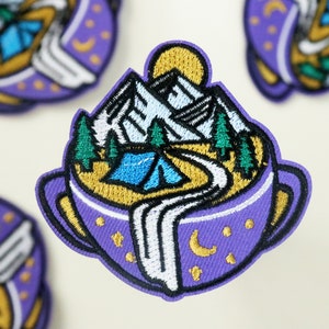 May include: Purple embroidered patch featuring a mountain scene within a mug. The mountains are white with a blue lake and a green tent. The mug has a white rim and a gold handle.