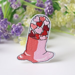 Puede incluir: Parche bordado para planchar de una píldora rosa y roja llena de corazones rosas y rojos.