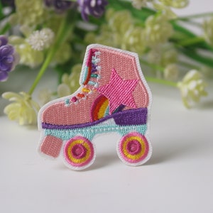 以下が含まれることがあります： 虹、星、黄色い車輪が付いたピンクのローラースケートの刺繍パッチ。