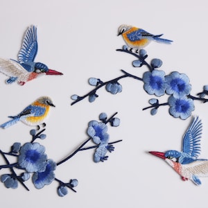 Op de afbeelding: Geborduurde patches met vogels en bloemtakken. De patches tonen blauwe, gele en witte vogels met rode snavels, zittend op of vliegend in de buurt van blauwe bloementakken. Ideaal voor het decoreren van kleding of accessoires.