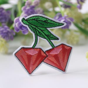 May include: Embroidered iron-on patch of two red cherries with green stems and leaves.
