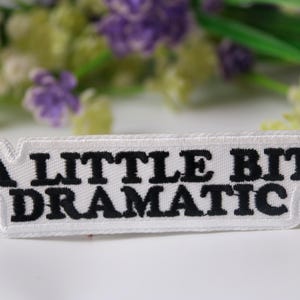 May include: White iron-on patch with black embroidered text that reads "A little bit dramatic".