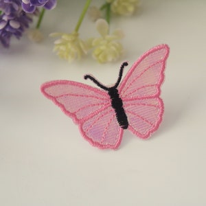 May include: A pink butterfly iron-on patch with black embroidered details. The patch is perfect for adding a touch of whimsy to clothing, bags, or other fabric items.
