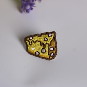 Könnte beinhalten: Ein gelber gestickter Bügelaufkleber mit einem Stück Schweizer Käse mit Löchern.