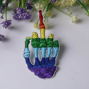 Könnte beinhalten: Bunt gestickter Bügelaufkleber mit einem Skeletthand, die den Mittelfinger zeigt.