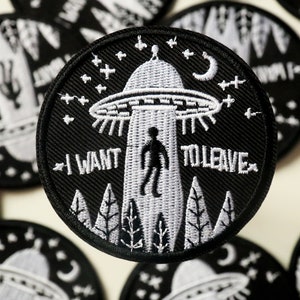 May include: Black and white embroidered patch with a UFO, a person, and the text "I WANT TO LEAVE".