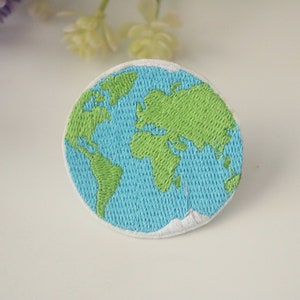 Puede incluir: Un parche bordado de la Tierra, con colores verde y azul. El parche es circular y tiene un borde blanco.