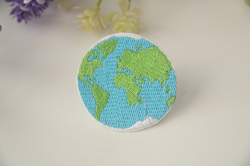Pode incluir: Um remendo bordado da Terra, com cores verde e azul. O remendo &eacute; circular e tem uma borda branca.