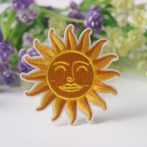 Pode incluir: Um remendo bordado amarelo com um sol sorridente e um contorno branco.