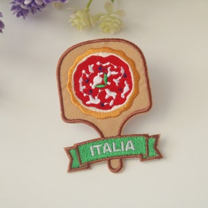 May include: Embroidered iron-on patch featuring a pizza on a wooden paddle with the word "ITALIA" on a green banner.