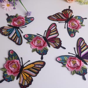 May include: Embroidered butterfly patches with colorful wings and pink flower accents. The patches feature various wing patterns in shades of blue, yellow, red, and purple. Decorative floral patches for crafts and apparel.