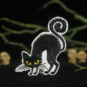 May include: Black embroidered iron-on patch of a black cat with yellow eyes. The cat is curled up in a sitting position with its tail wrapped around its body.