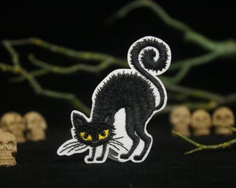 Op de afbeelding: Zwarte geborduurde strijkpatch van een zwarte kat met gele ogen. De kat zit opgerold met zijn staart om zijn lichaam gewikkeld.
