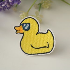 Puede incluir: Parche bordado de pato amarillo con gafas de sol. El pato tiene un pico naranja y está delineado en negro. El parche está bordeado con blanco, un accesorio divertido para ropa o bolsos.