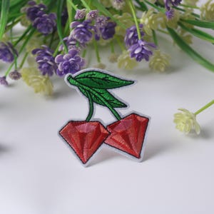 May include: Red embroidered cherry patch with green leaves. The patch is on a white background.