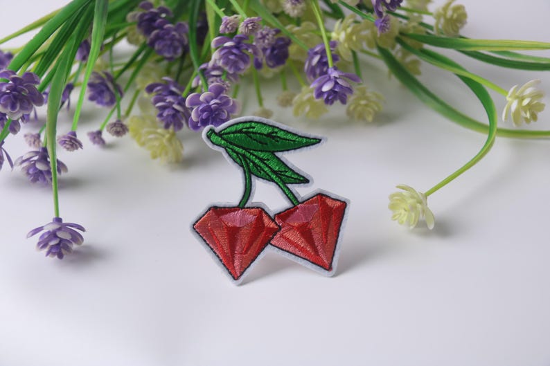 May include: Red embroidered cherry patch with green leaves. The patch is on a white background.