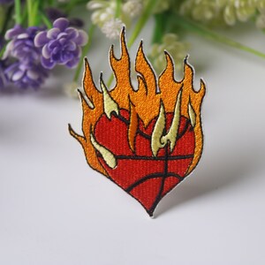 Puede incluir: Parche bordado para planchar con un balón de baloncesto en forma de corazón rojo en llamas. Las llamas son de color naranja y amarillo.