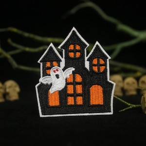 May include: A black and orange embroidered patch of a haunted house with a ghost flying out of a window. The house has orange windows and a white trim.