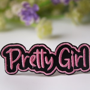 Może przedstawiać: Różowa haftowana naszywka z tekstem "Pretty Girl" w czarnym konturze.