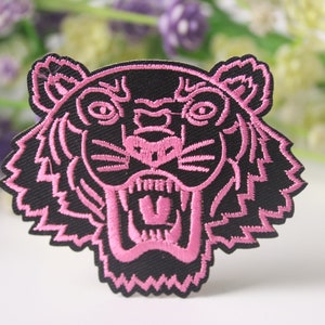 Puede incluir: Parche de cabeza de tigre bordado en rosa con contorno negro.