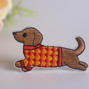May include: Embroidered iron-on patch of a brown dachshund wearing a red and yellow sweater.