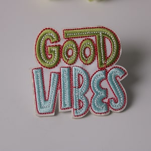 Puede incluir: Parche bordado para planchar con el texto "Good Vibes" en letras verdes, azules y rojas.