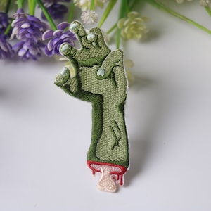 Op de afbeelding: Groene zombiehand met rood druppelend bloed, geborduurd strijk-patch.