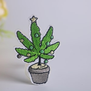 May include: Green embroidered patch of a marijuana plant shaped like a Christmas tree with a star on top, in a gray pot.