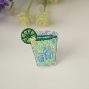 May include: Embroidered iron-on patch of a green glass with ice cubes and a lime wedge.