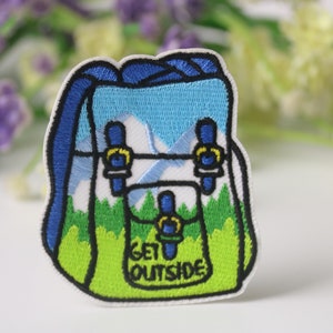 May include: Embroidered iron-on patch featuring a cartoon backpack with a mountain scene and the text "GET OUTSIDE".