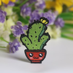 Può includere: Un cactus verde con un fiore giallo in cima, in un vaso rosso con un viso carino. Il vaso ha un contorno nero.