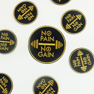 Puede incluir: Parches bordados en negro y dorado con el texto "NO PAIN NO GAIN" y un diseño de barra con pesas. Los parches redondos están dispersos sobre un fondo blanco, para entusiastas del fitness.