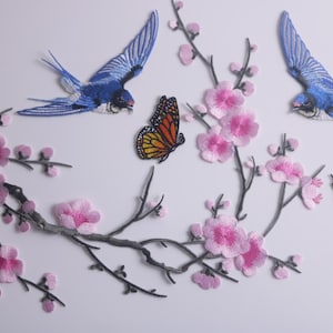 Puede incluir: Parches bordados para planchar con una rama de cerezo rosa, dos golondrinas azules y dos mariposas naranja y negras.