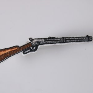 May include: An embroidered patch depicting a rifle with a wooden stock, in black and brown.