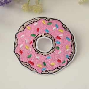 Könnte beinhalten: Rosa gestickter Donut-Patch mit bunten Streuseln.