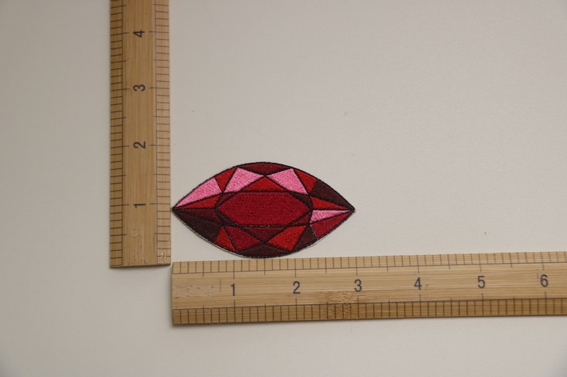 May include: An embroidered gem patch in red and pink. The gem is teardrop shaped and has a faceted design.