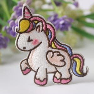 May include: Embroidered iron-on patch featuring a cartoon unicorn with a pink, yellow, and blue mane and tail. The unicorn has a white body with brown outlines and pink hooves.