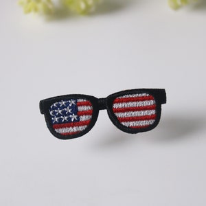 May include: A black and white embroidered patch of sunglasses with the American flag design in the lenses.