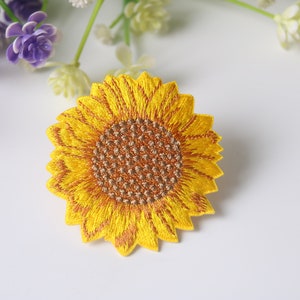 Puede incluir: Un parche bordado de girasol amarillo con un centro marrón. El parche es perfecto para agregar un toque de naturaleza a la ropa, las bolsas u otras manualidades.