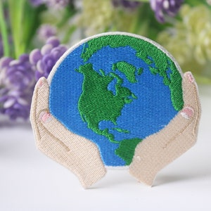 May include: Embroidered patch of two hands holding a blue and green globe. The globe is a representation of the Earth.