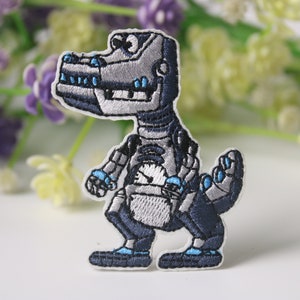 Puede incluir: Un parche de hierro bordado de color plateado y azul de un dinosaurio robot. El dinosaurio tiene un reloj en el pecho y está de pie sobre dos piernas.