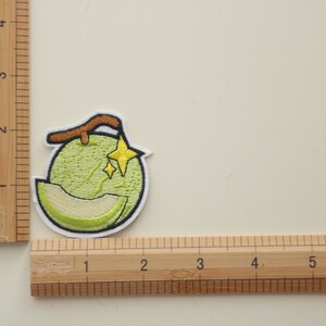 Peut inclure: &Eacute;cusson brod&eacute; repr&eacute;sentant un melon vert avec une tranche coup&eacute;e, une tige marron et deux &eacute;toiles jaunes. L'&eacute;cusson a une bordure blanche, id&eacute;al pour les v&ecirc;tements ou accessoires.